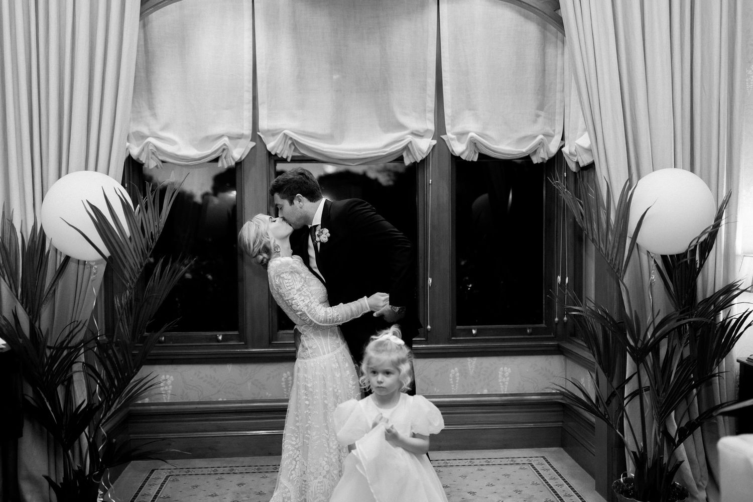 An intimate wedding moment captured in black and white photography with elegant window drapes and decor.