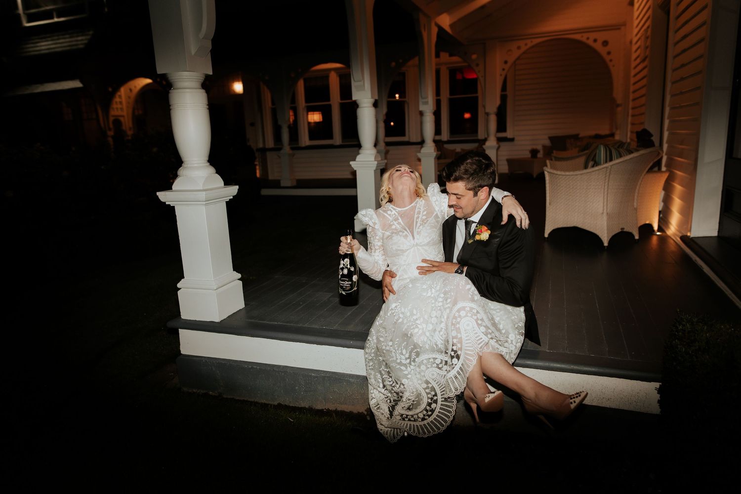Couple shares an intimate evening moment while sitting on outdoor porch steps in elegant evening attire.
