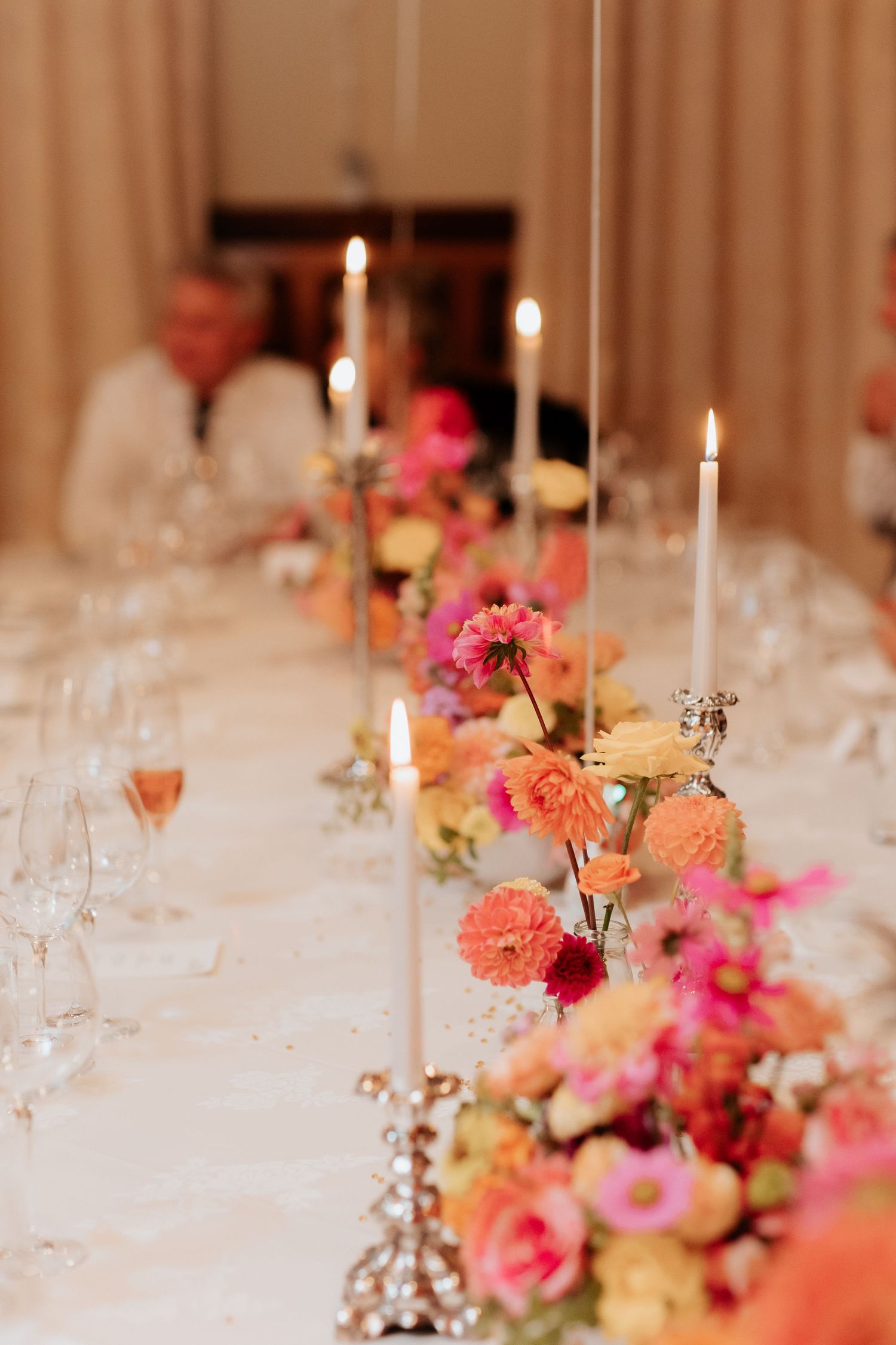 Elegant dining table with candlesticks and pink and peach floral centerpieces on white tablecloth for wedding reception.