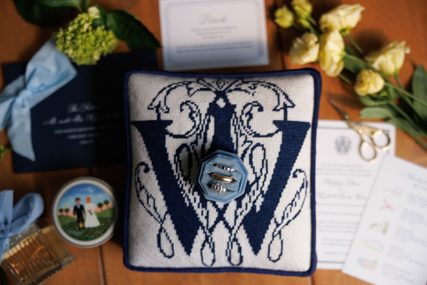 Wedding details flatlay with blue and white decorative pillow and yellow roses.