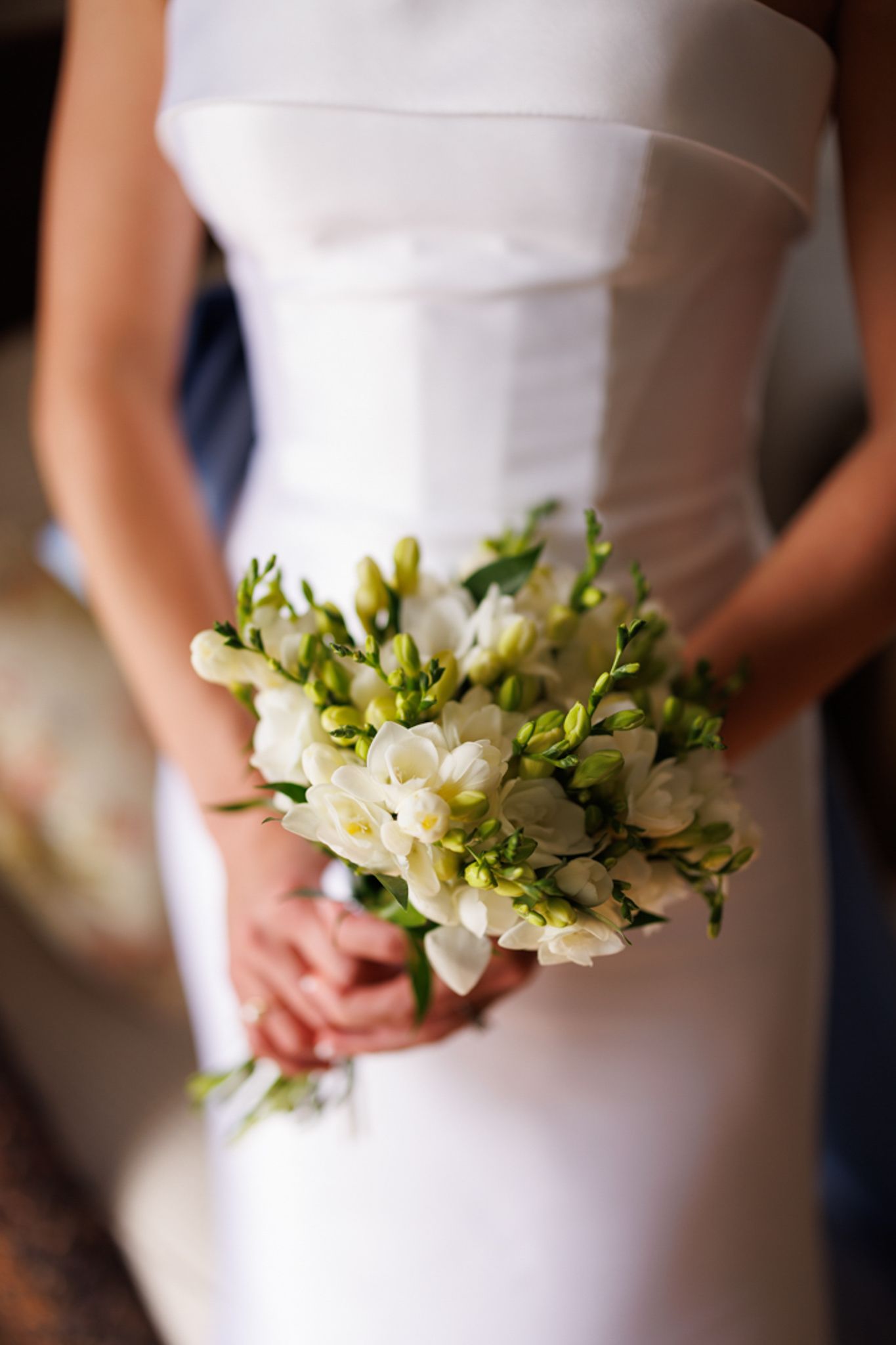 White and green bridal bouquet held against elegant wedding dress.