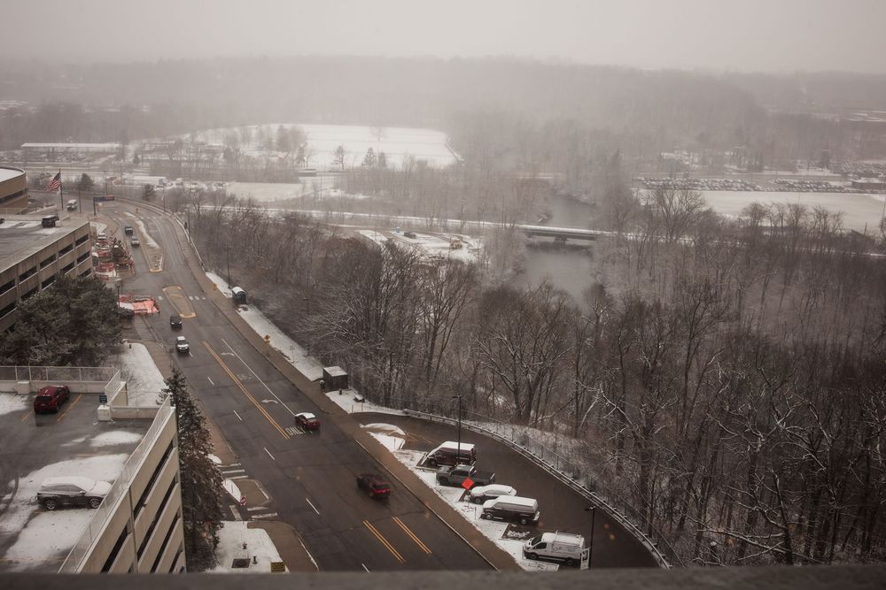 Aerial view of snowy landscape with roads and parked cars visible.
