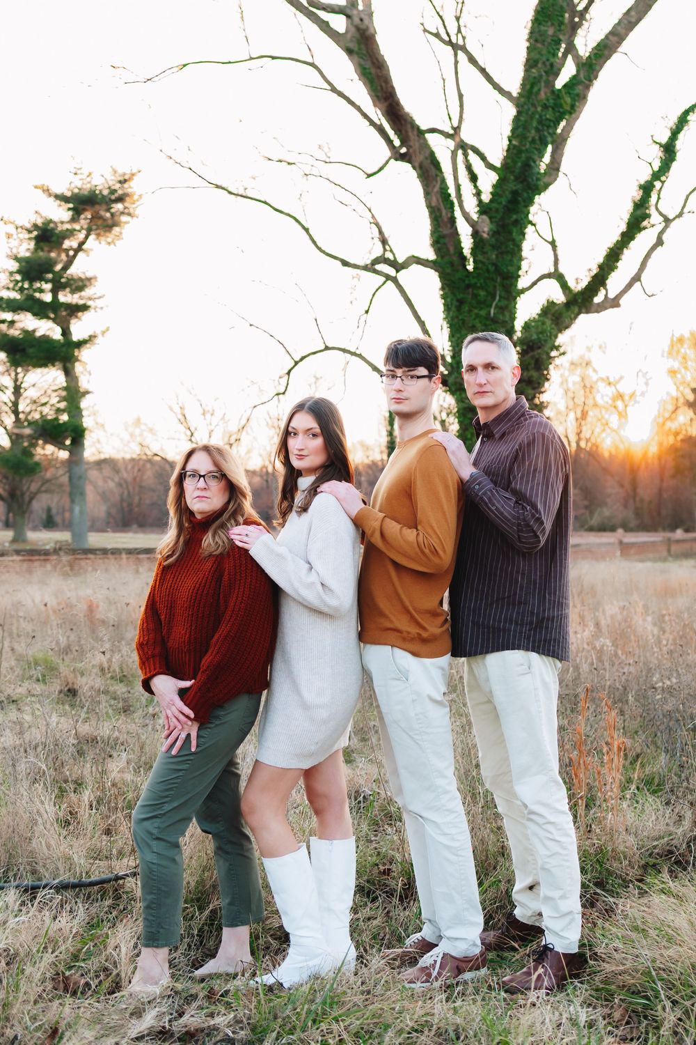 Family of four posing outdoors at sunset near a moss-covered tree in a golden field.
