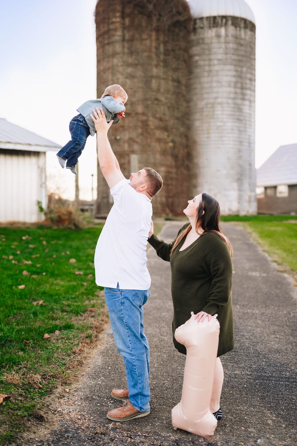 Family plays together near farm silos as parent lifts child high into the air.