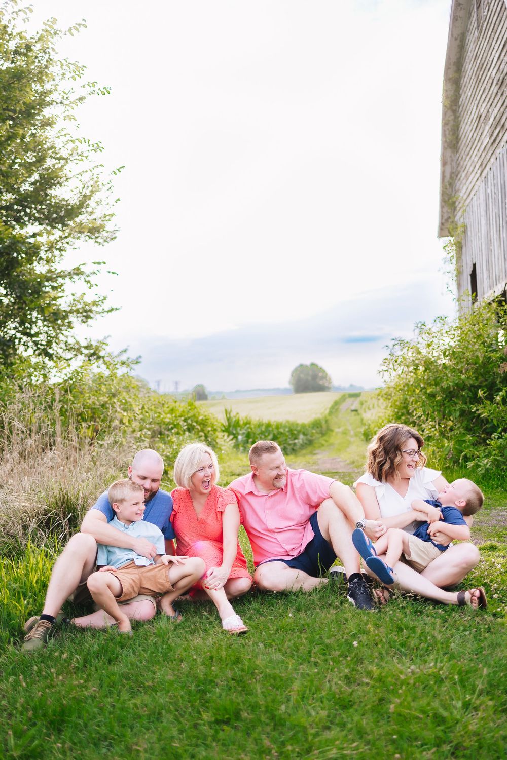 Extended family relaxing together on grassy hill by rustic barn.
