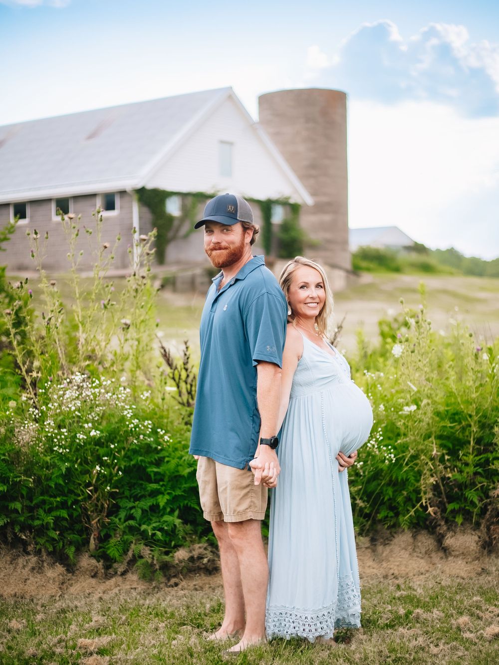 Rural maternity photo with barn and silo in the background on a sunny day.