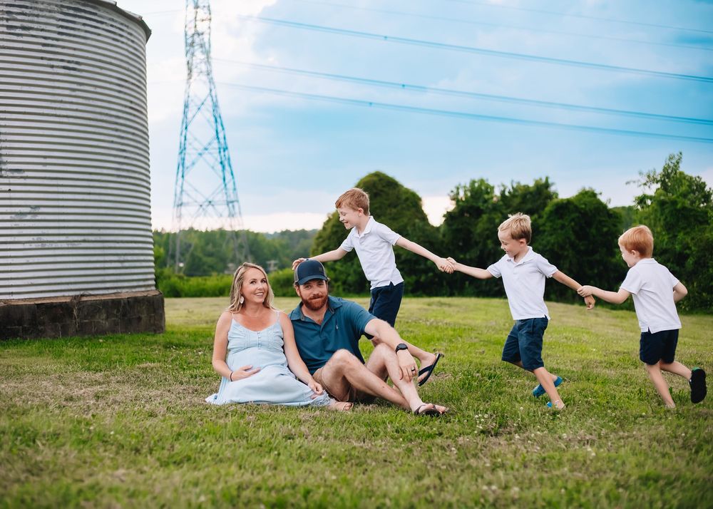 A joyful family scene in a countryside setting with a grain silo and children playing in a grassy field.