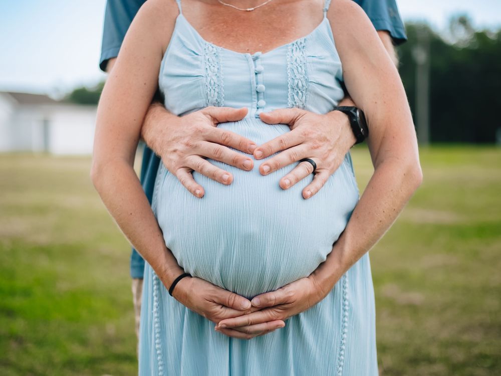 Closeup of hands cradling a pregnant belly in a light blue maternity dress.