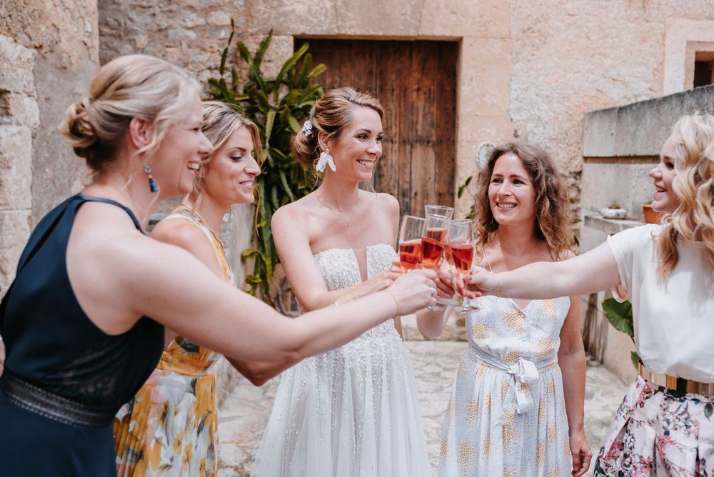 Eine Gruppe elegant gekleideter Hochzeitsgäste erhebt im Innenhof der Finca Xiclati auf Mallorca ihre Gläser zu einem feierlichen Toast.