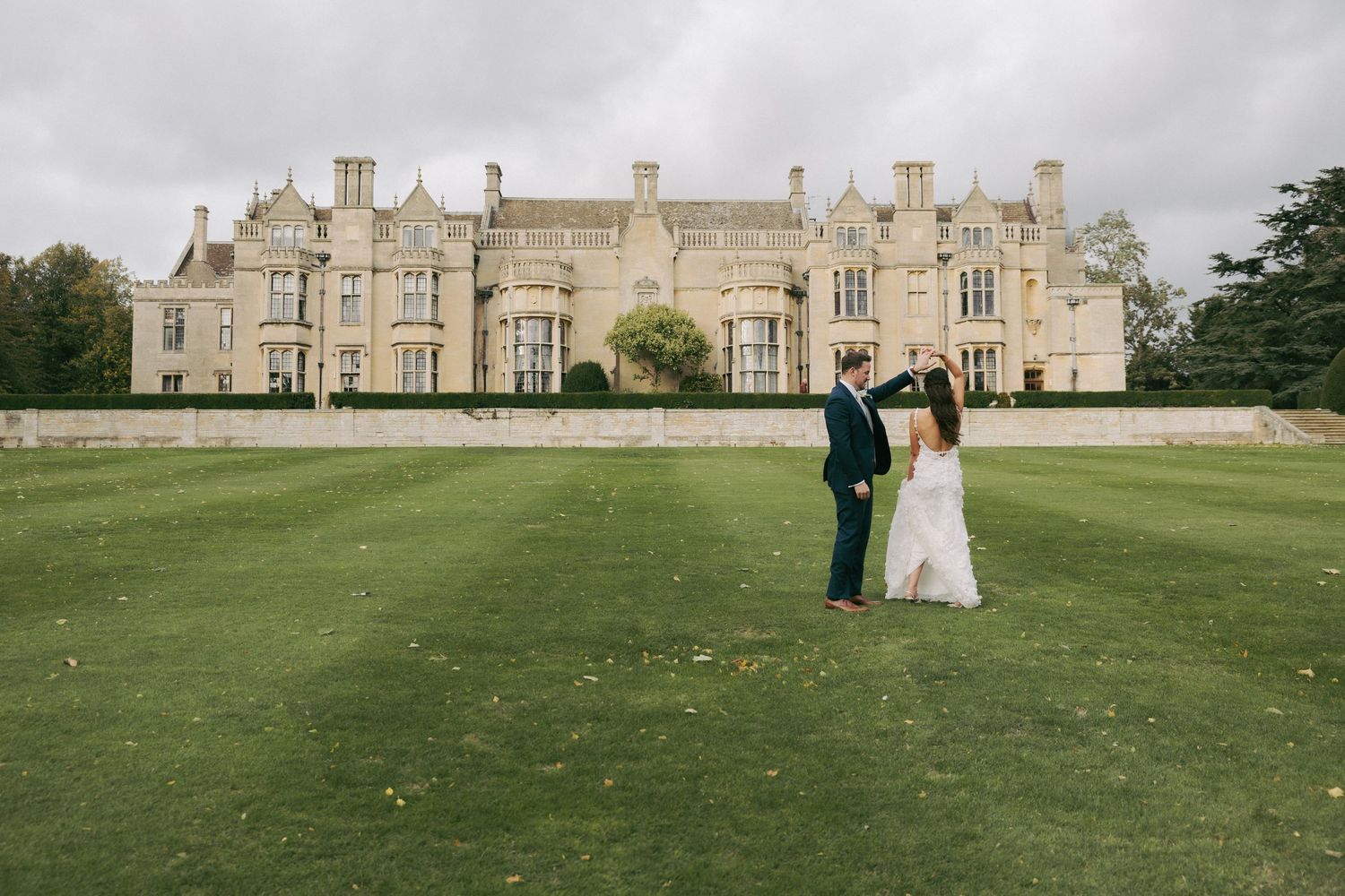 Elegant stone mansion with manicured lawn serves as backdrop for outdoor wedding photography.