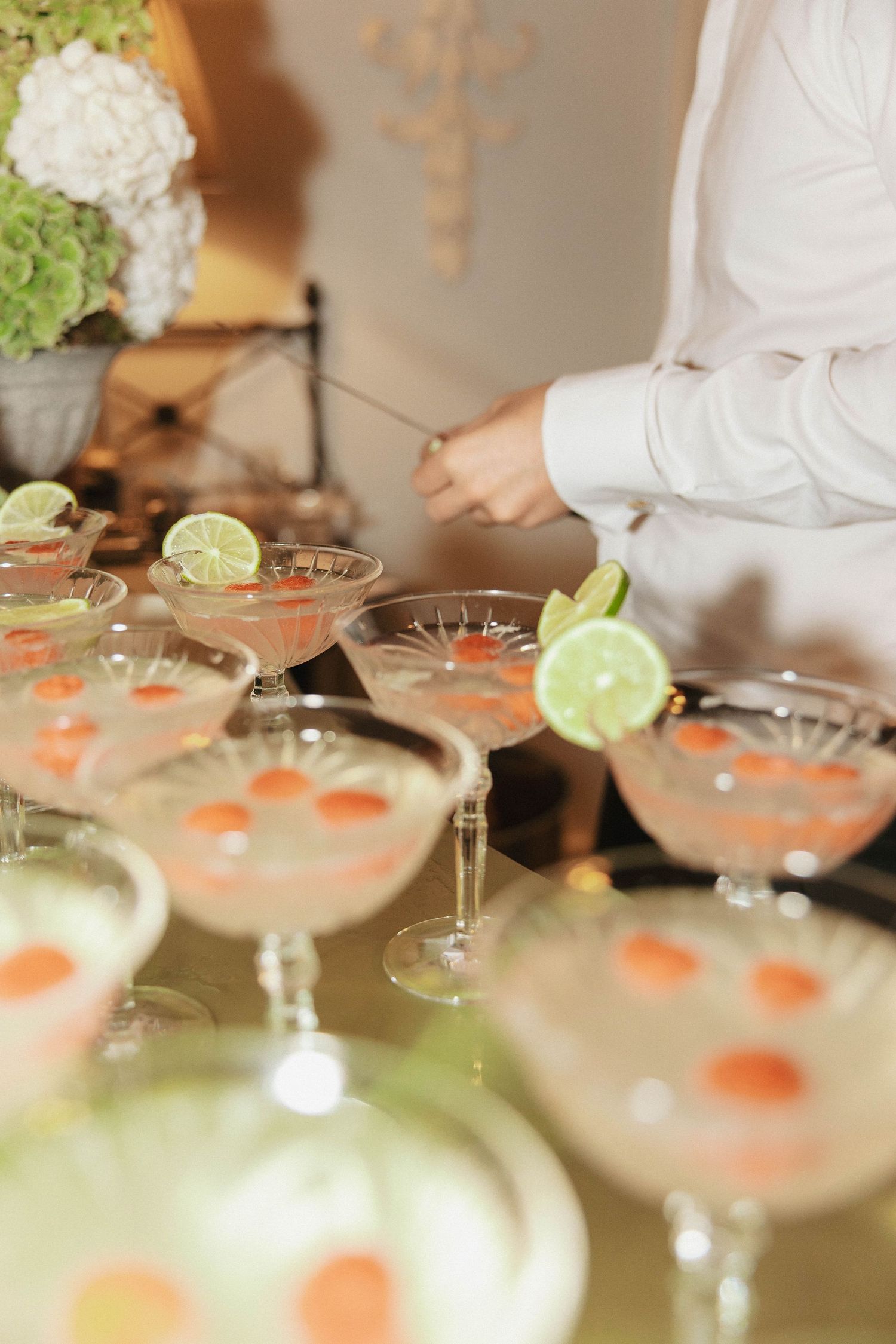 Elegant cocktail glasses garnished with lime slices and orange dots arranged on a mirrored surface at a catered event.
