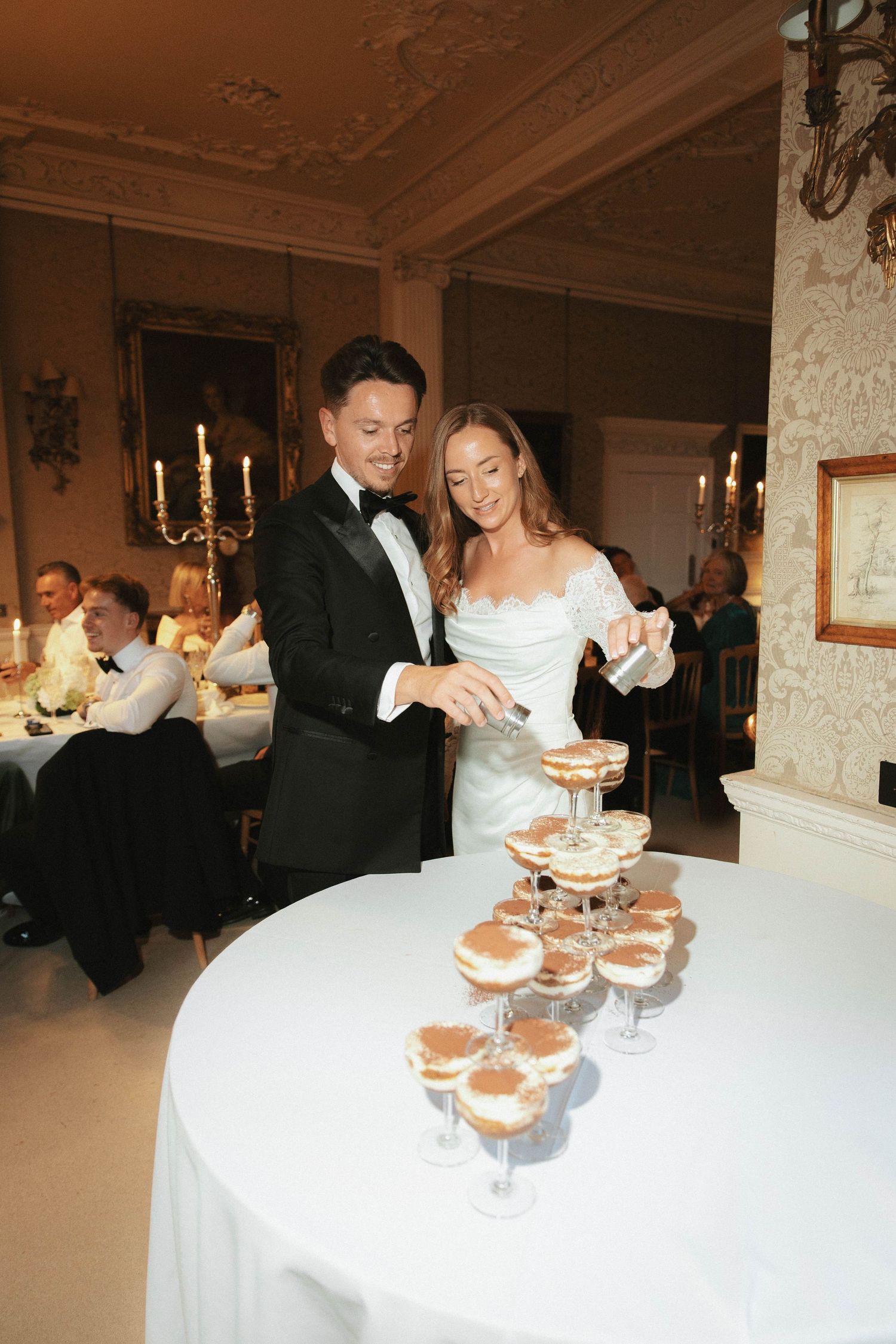 Bride and groom cutting tiramisu tower cake at elegant wedding reception in ornate venue.