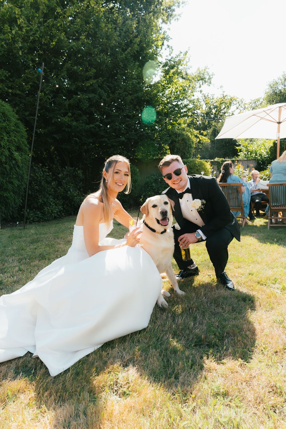 A couple in wedding attire plays with their dog on grassy hill during an outdoor photo session.