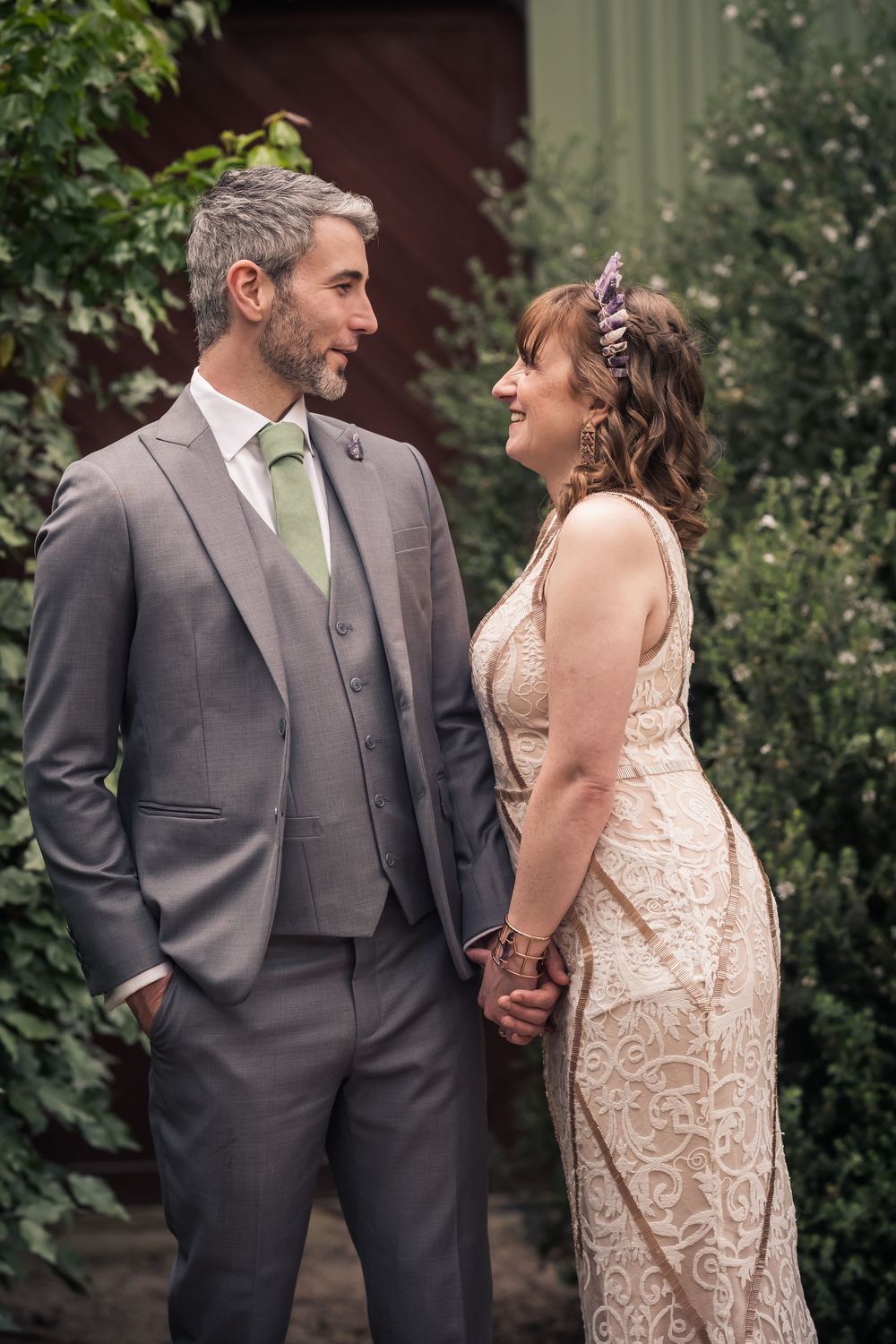 A couple in wedding attire share intimate moments in a garden setting wearing gray suit and cream lace dress.