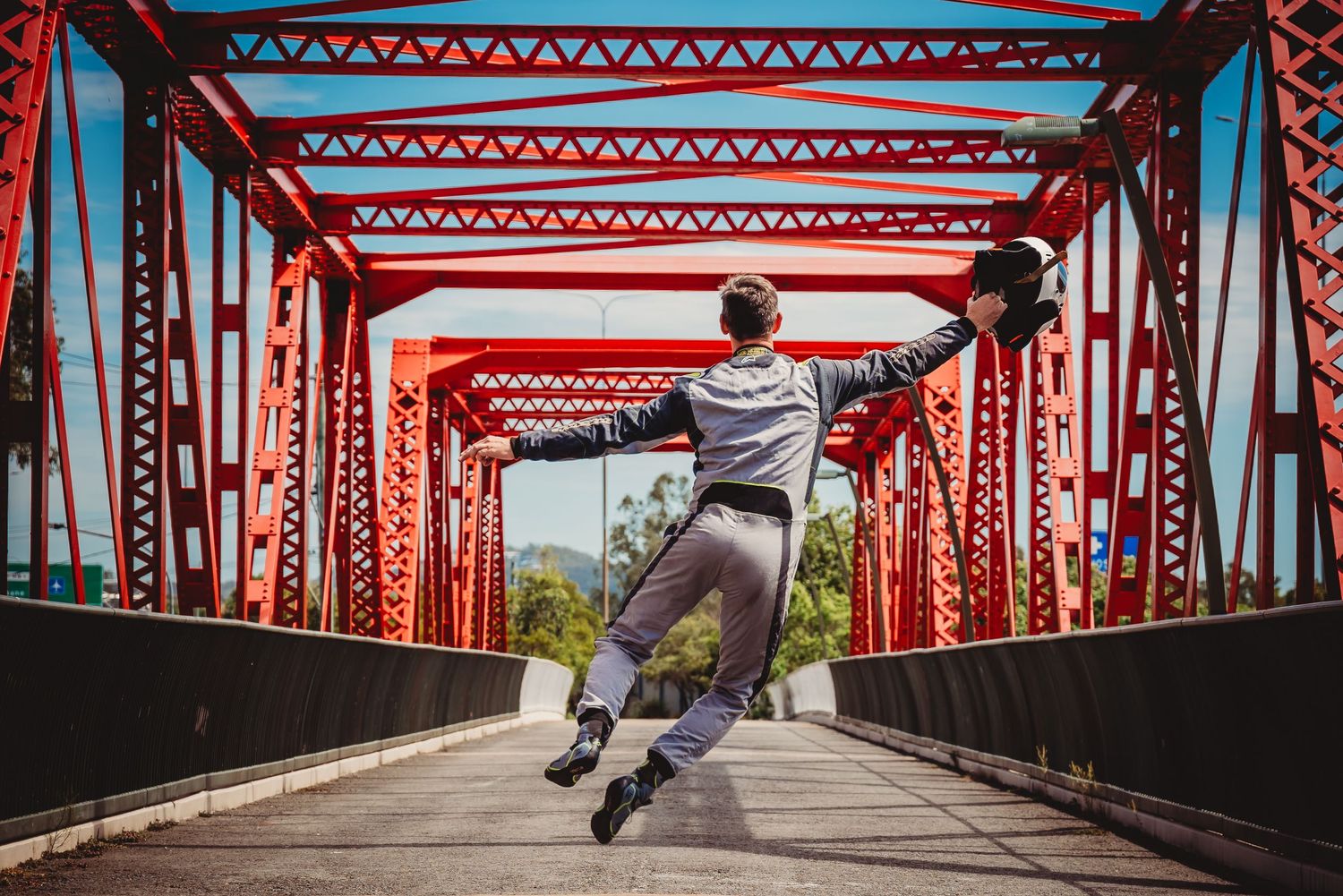 Person dribbles basketball on red metal bridge walkway with geometric patterns and supports.