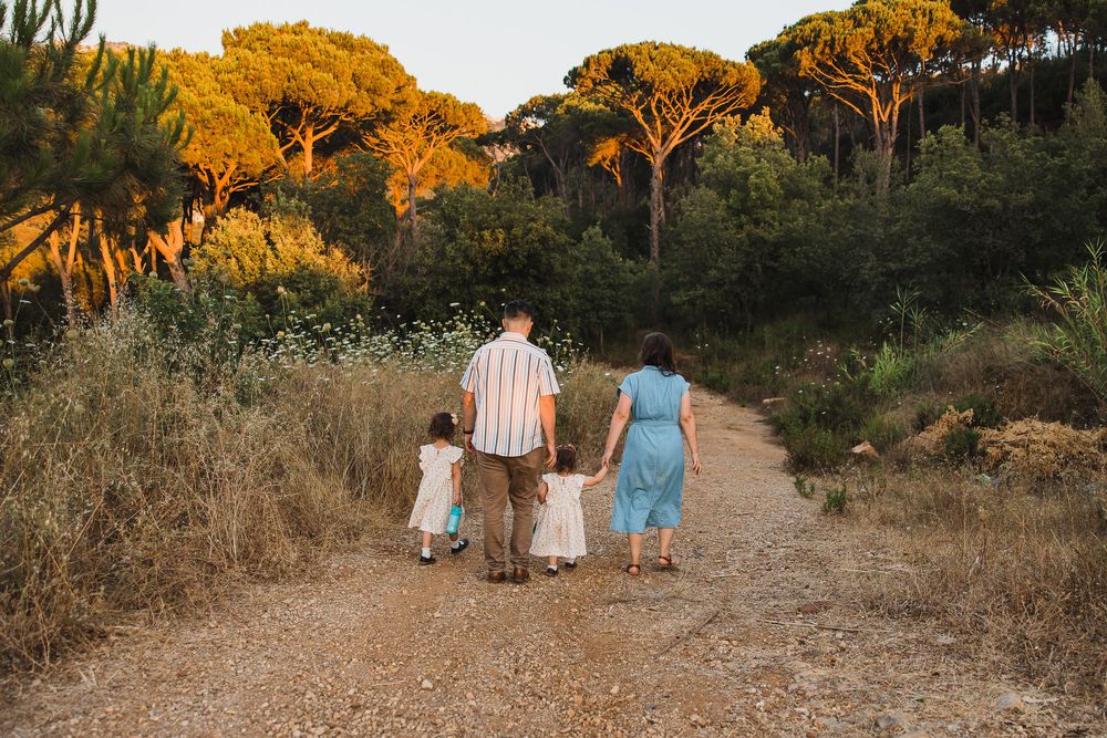 People walking on a dirt path at sunset with golden pine trees illuminated in warm evening light.