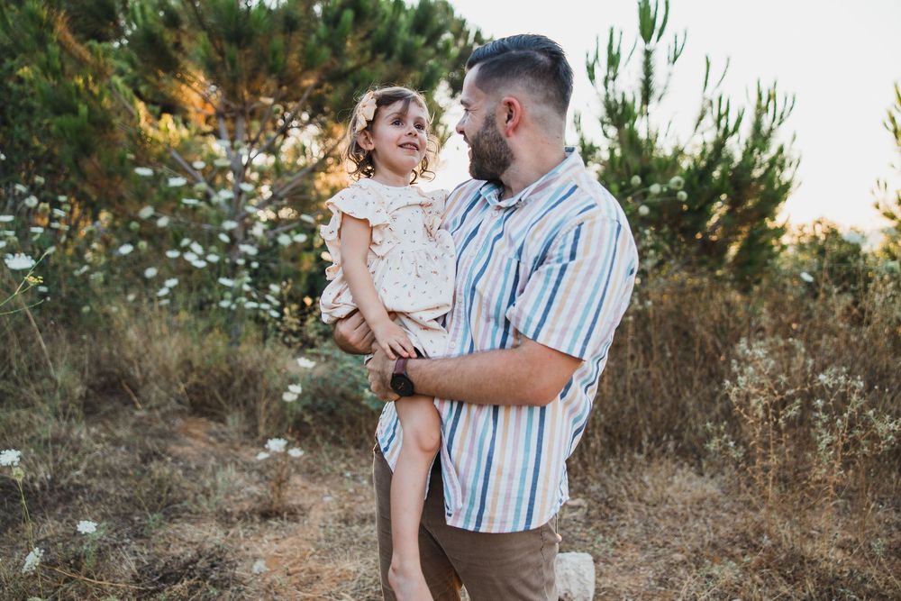 A parent and child share a tender moment together outdoors among pine trees at sunset.