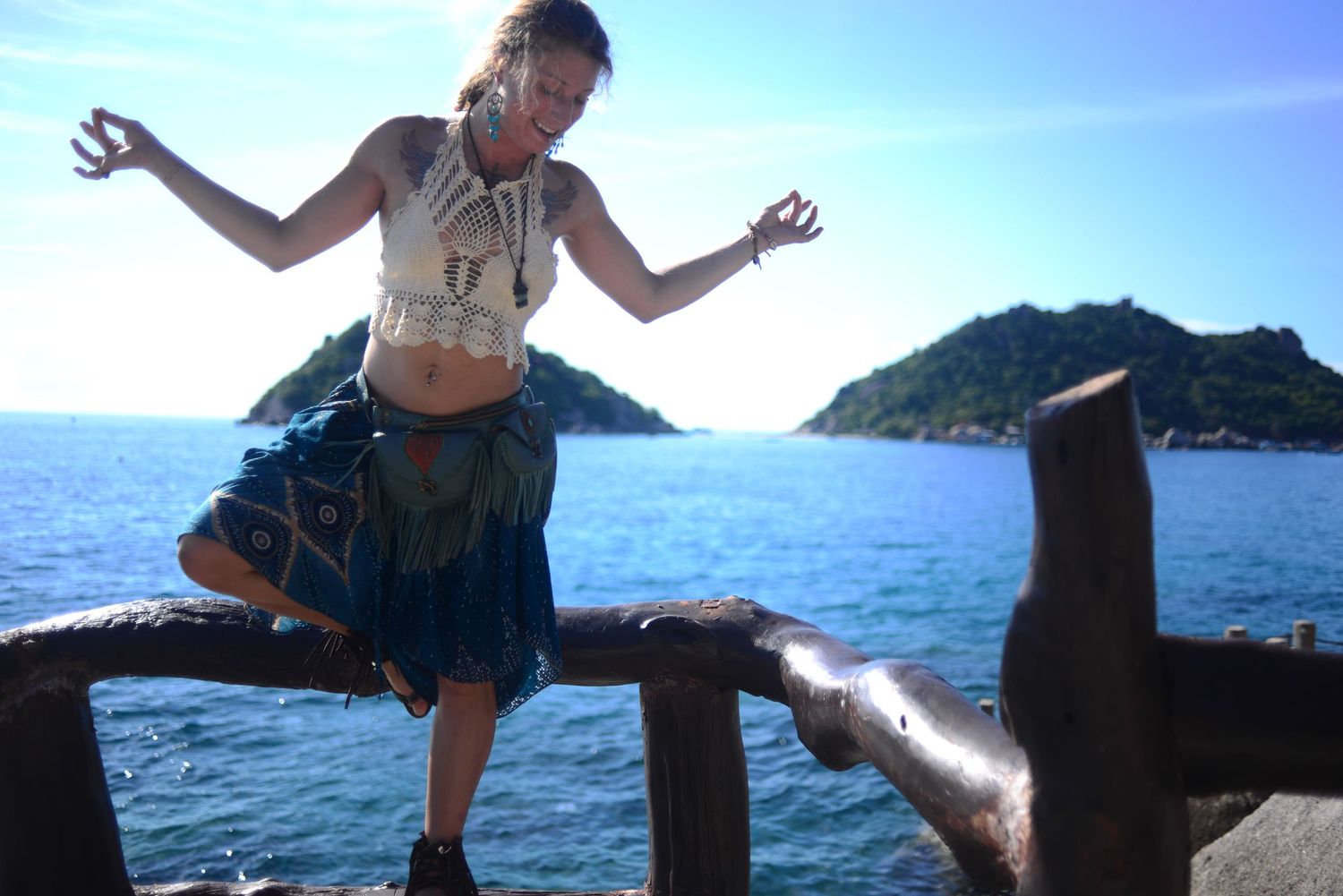 A person jumps off a wooden pier into the serene blue ocean water with mountains in the background.