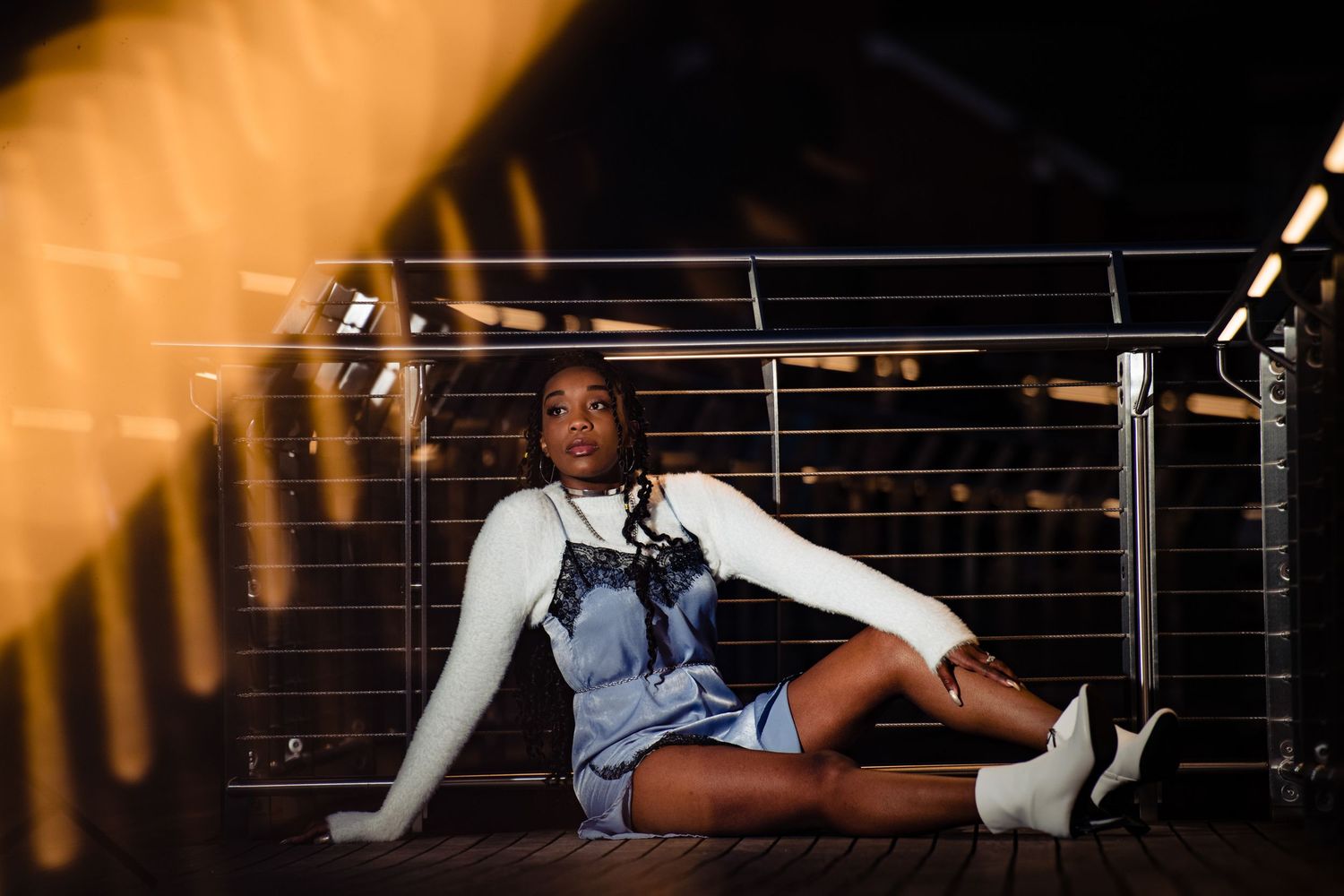 Legs of multiple people dangle over edge in dark lit environment with railings visible in background.