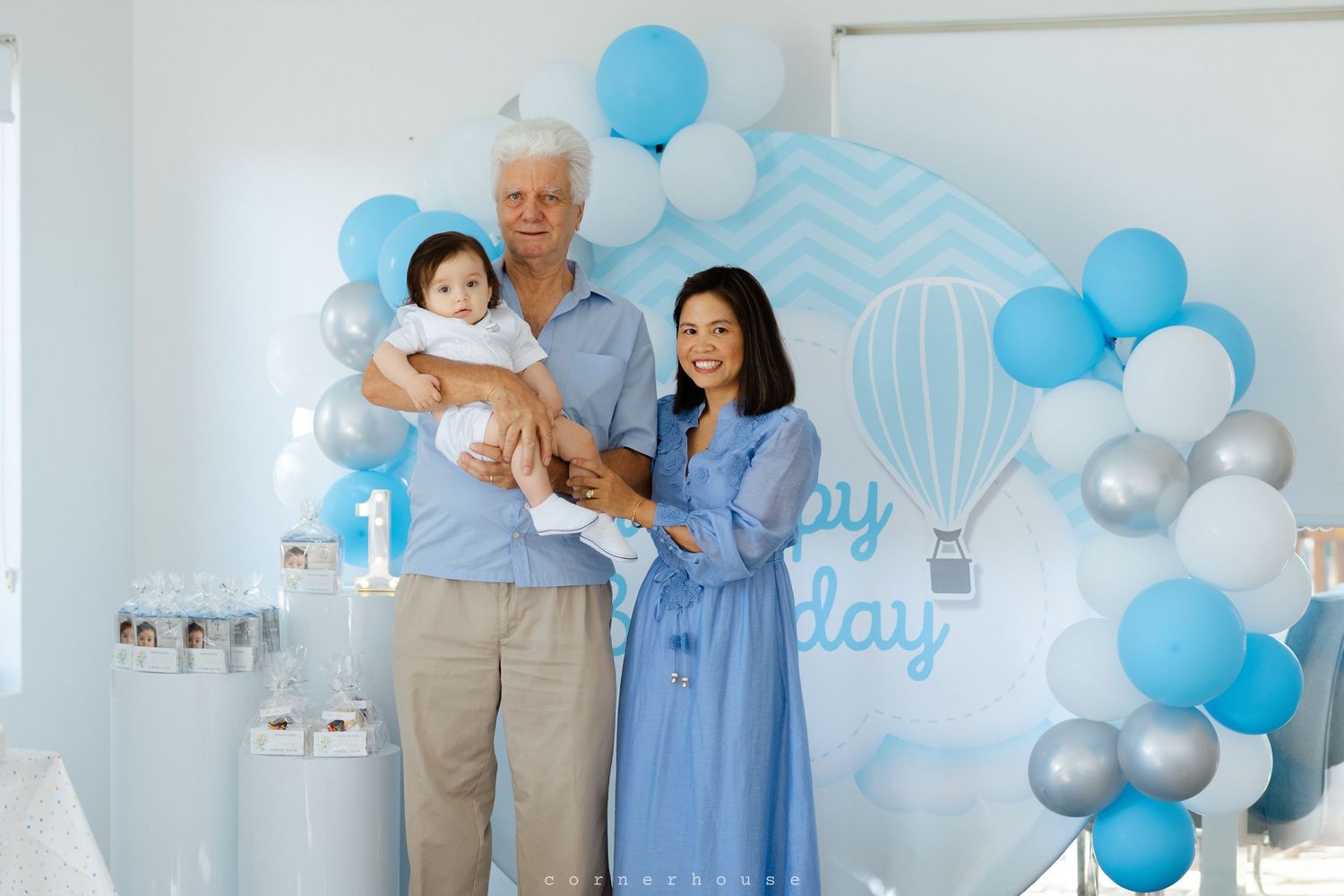 Baby shower celebration with blue and white balloon decorations and people in coordinating blue and beige outfits.