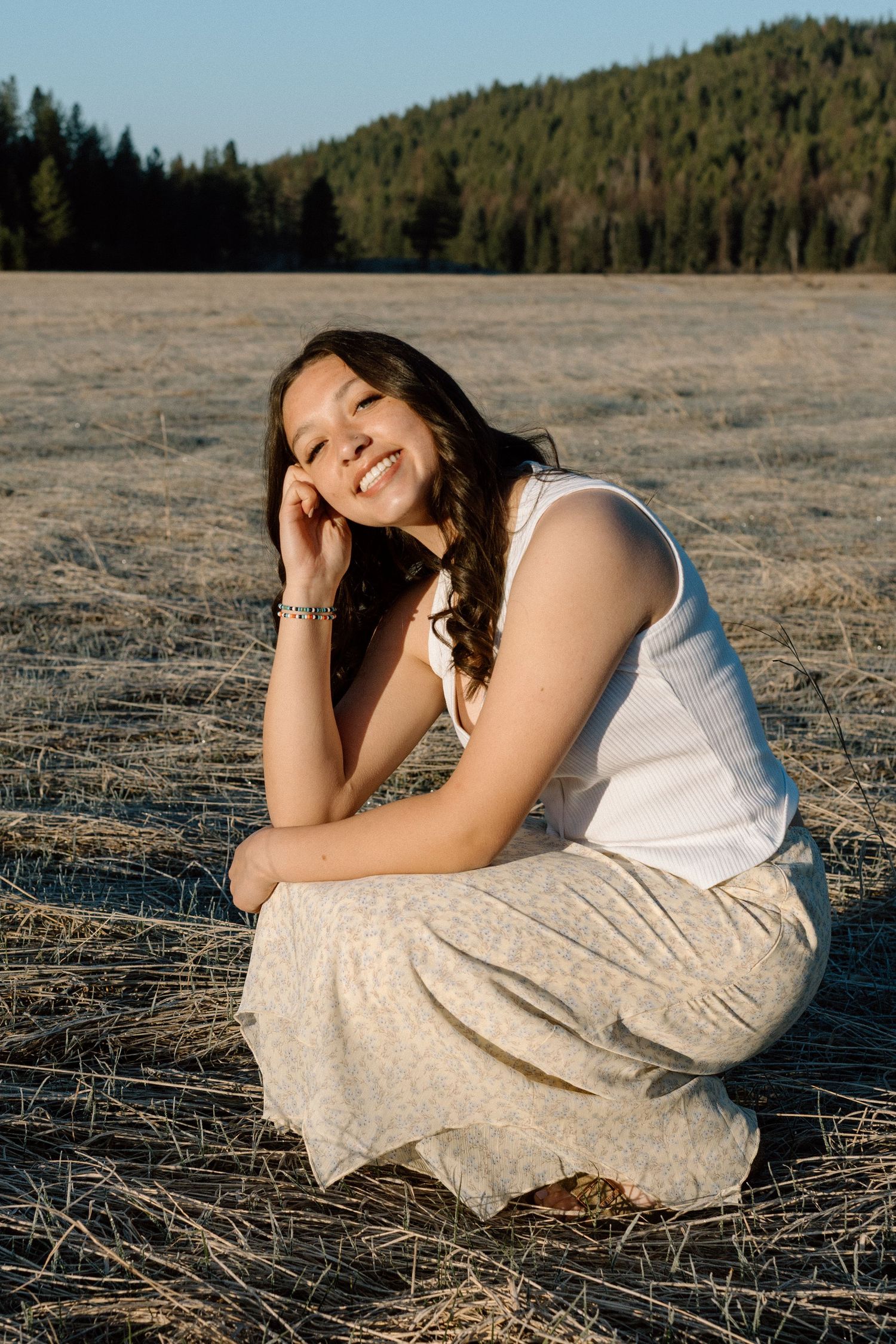 Artistic portrait on dry grass field with mountains and forest in background.