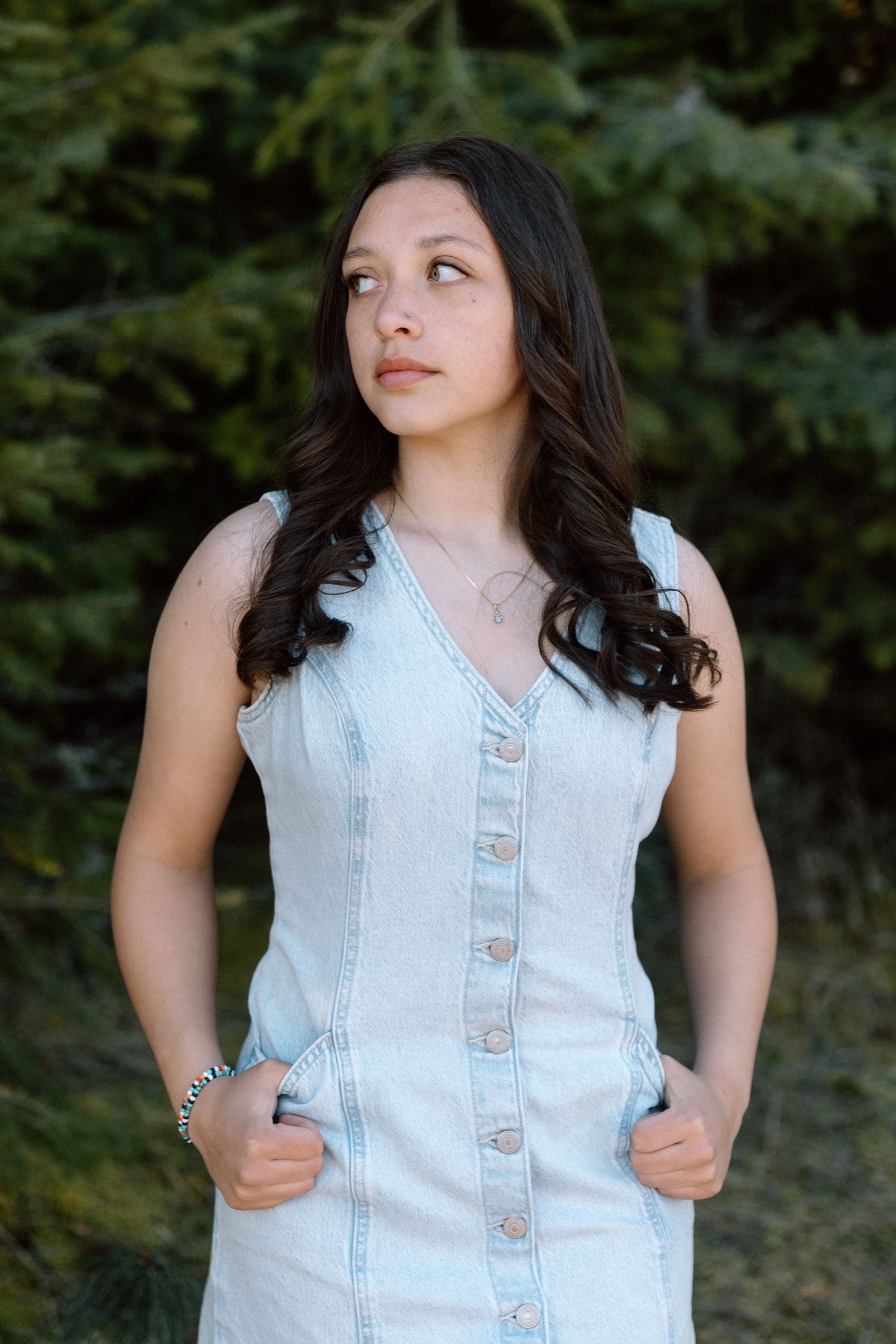 Portrait shot featuring light denim dress against evergreen forest backdrop.