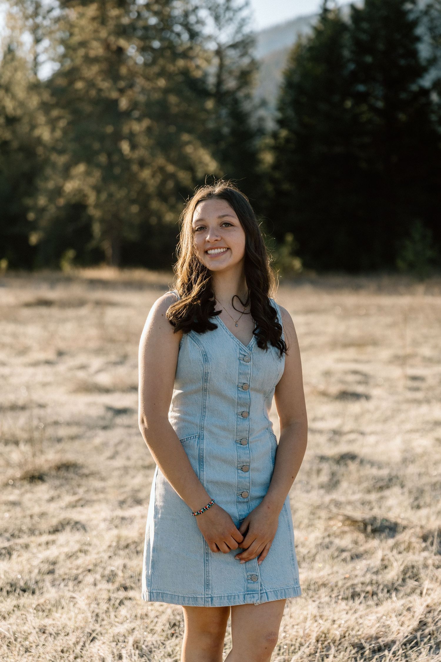 Casual denim dress outfit photographed in golden sunlight with forest backdrop.
