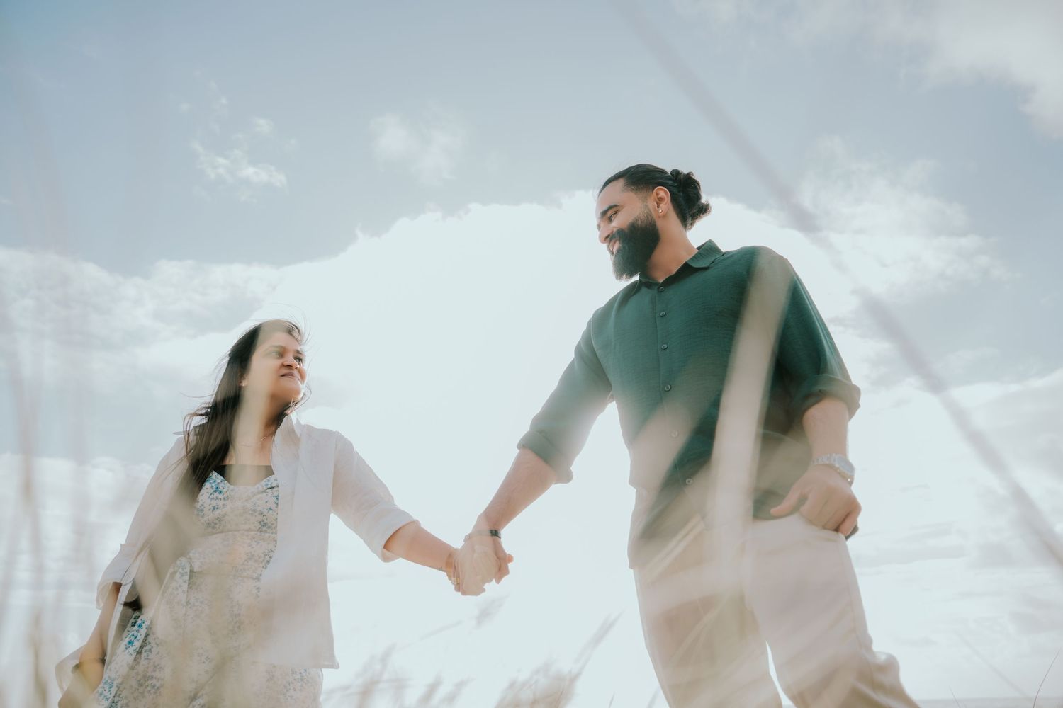 Couple sitting together in tall beige grass on a romantic outdoor photoshoot.