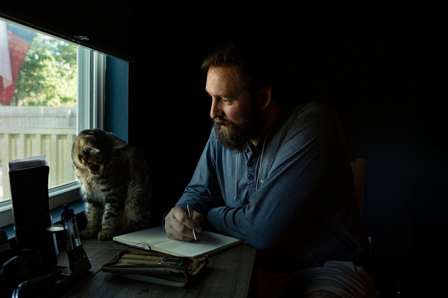 A person sits at a desk in a dimly lit room looking at a computer screen while working. Photographed by Jon Rock
