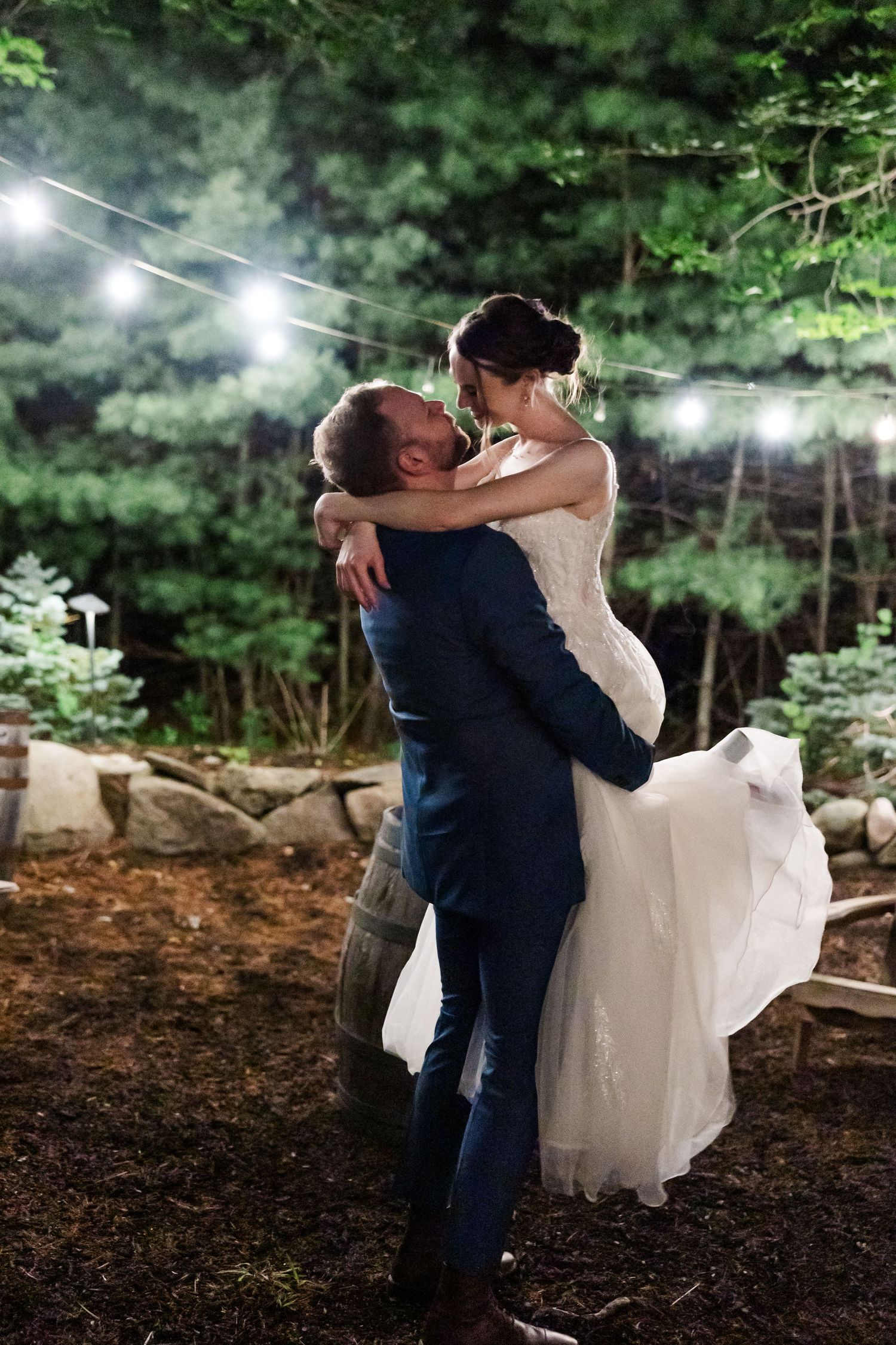 A couple shares an intimate moment during their woodland wedding celebration as string lights twinkle overhead.