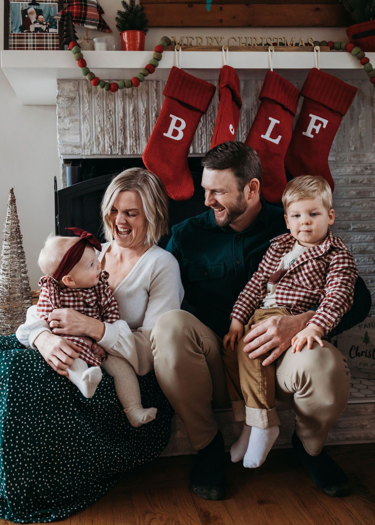 A family wearing matching red holiday sweaters sits together at a table decorating gingerbread houses for Christmas.