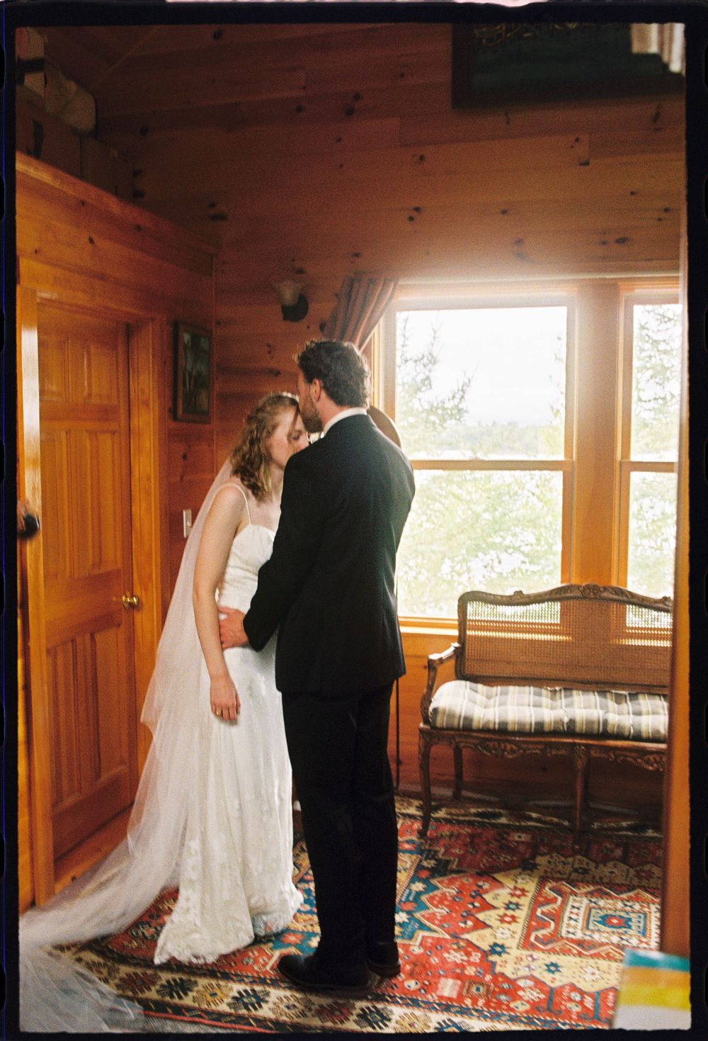 Groom kisses the forehead of bride to be during intimate first look on 35mm film at summer wedding in Brooklyn, Maine.