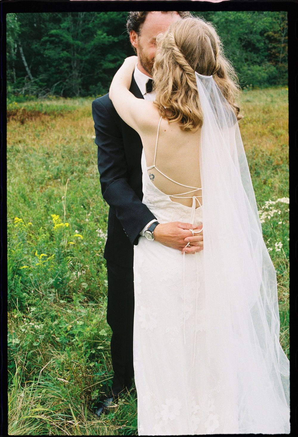 Couple embraces in a field before their wedding ceremony on 35mm color film during the summer in Downeast Brooklyn, Maine.