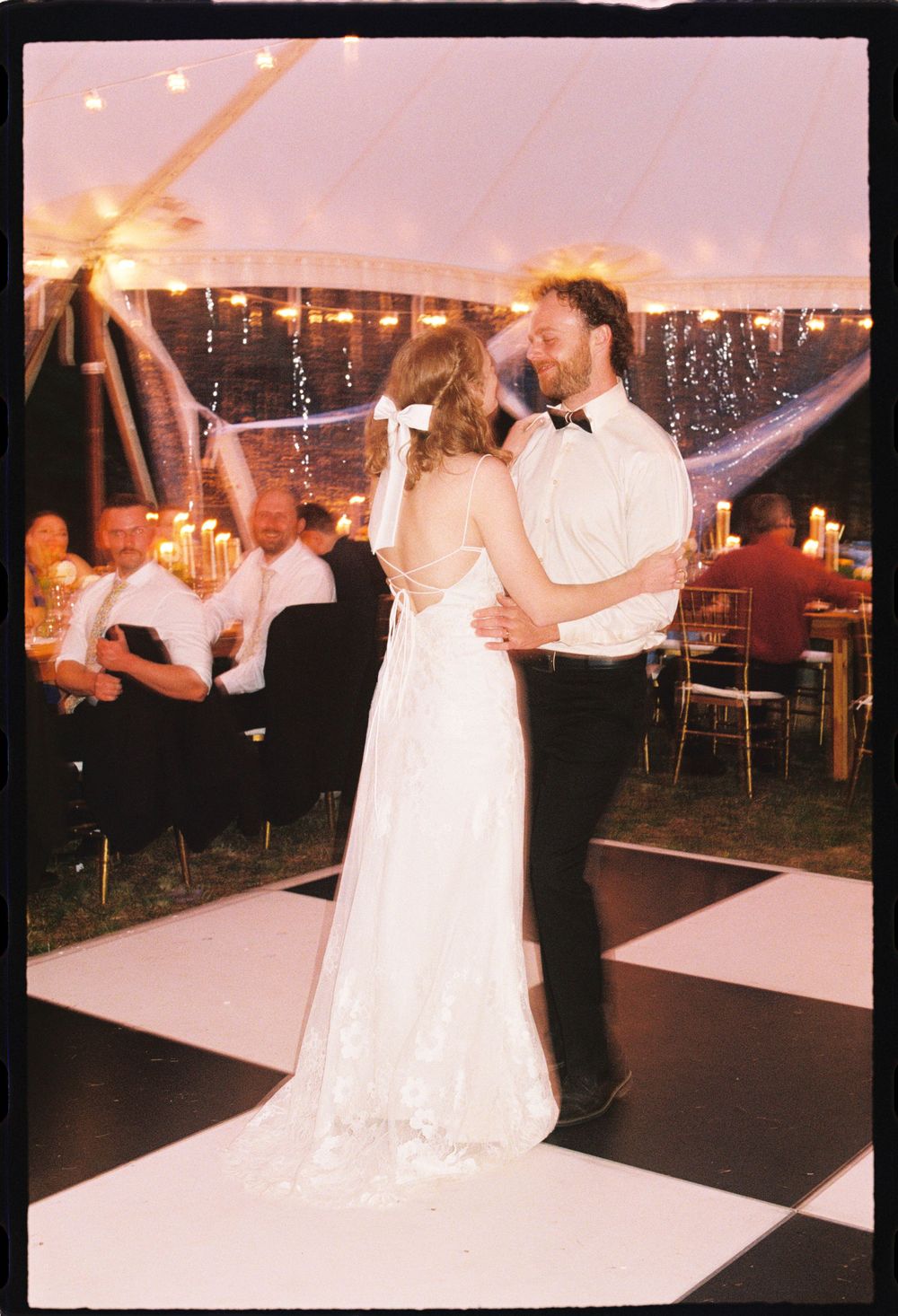 Bride and groom laughing and smiling together during their first dance on a checkered floor in the tent celebrating their wedding reception.