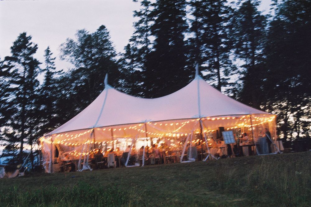 Landscape photo of the wedding reception tent lit up by string lights as the sun sets on 35mm film during this midcoast summer wedding.