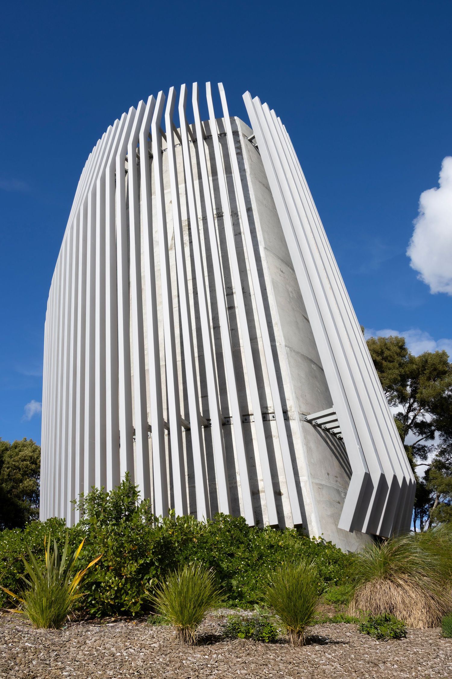 Sculptural concrete tower wrapped in white vertical fins, set against a deep blue sky.