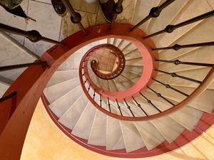 Looking up at a spiral staircase with wooden railing and cream-colored steps creating a mesmerizing architectural pattern.