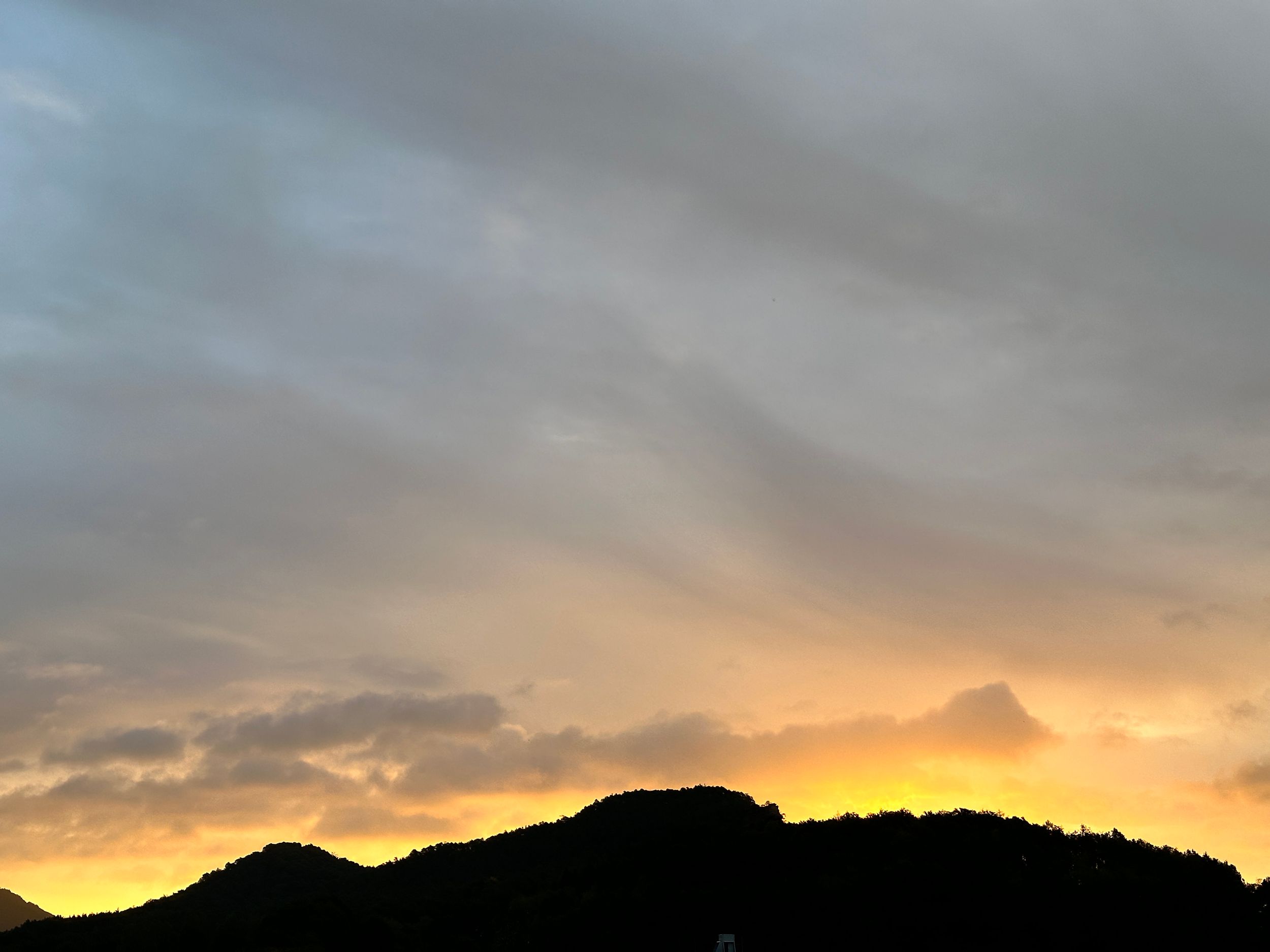 Mountain silhouette against vibrant golden sunset with dramatic cloudy sky above.