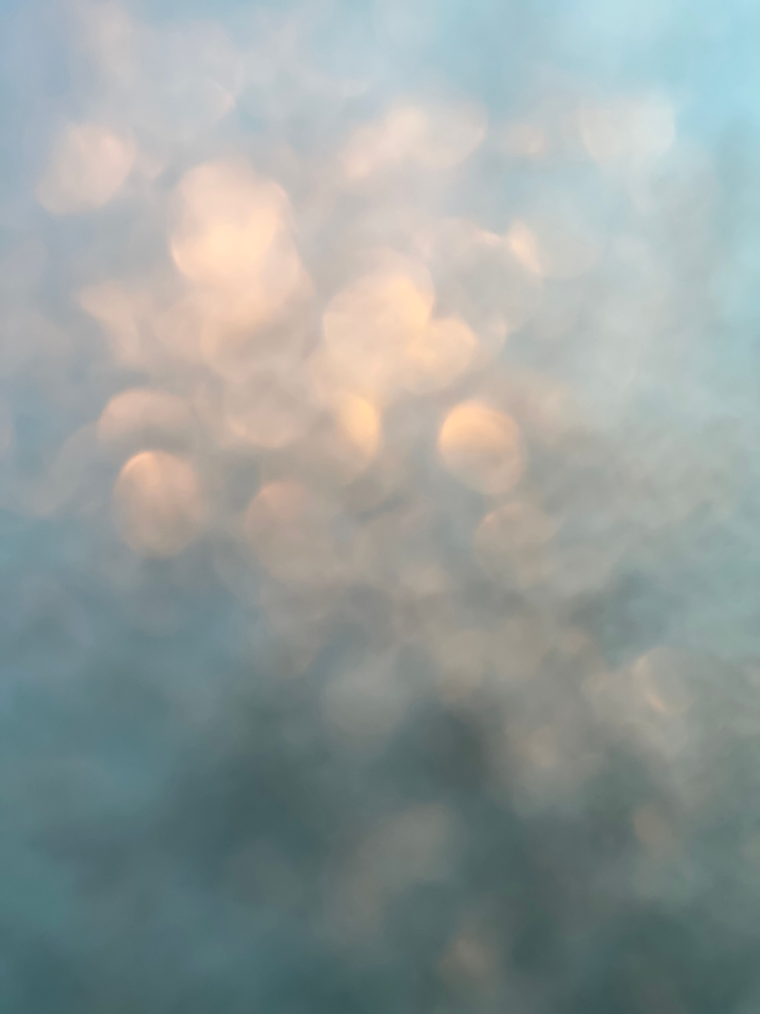 Ethereal pastel clouds with glowing orbs create a dreamy bokeh effect against a soft blueish-gray sky at sunset.