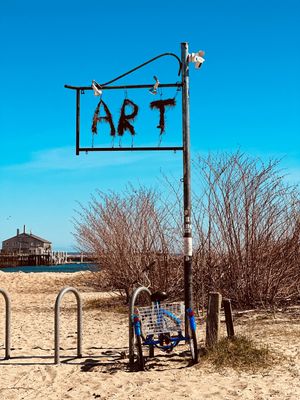 A sequence of playground equipment on sandy beach with bare bushes and blue sky in the background.