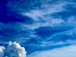 Wispy cirrus clouds streak across a deep blue summer sky with fluffy cumulus clouds on the horizon.