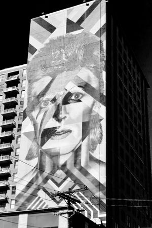Black and white urban street art mural depicting abstract geometric shapes and portrait elements on a city building.