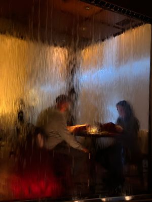 Silhouettes of people dining behind a foggy window with warm ambient lighting creating a moody atmosphere.