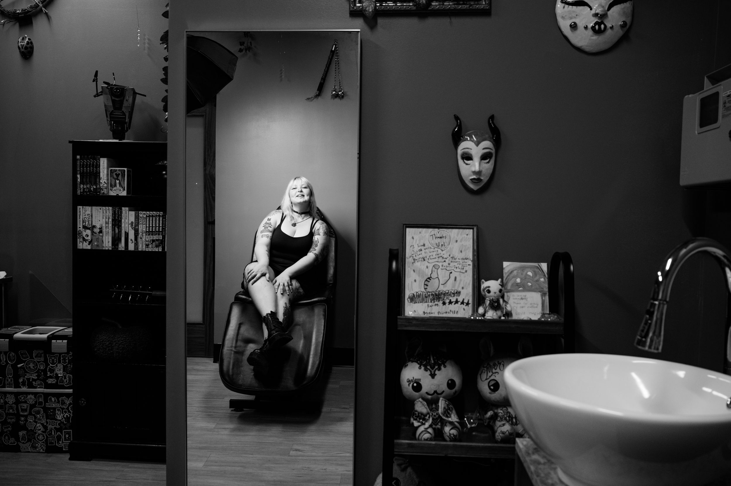 Black and white interior view of a massage chair near a wall decorated with decorative masks and shelving.