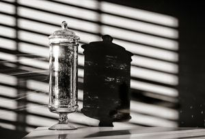 Light and shadow patterns from window blinds create dramatic lines and contrast on white wall with small decorative objects.
