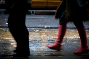 A person wearing red rain boots walks through puddles during a rainy day on a reflective wet surface.