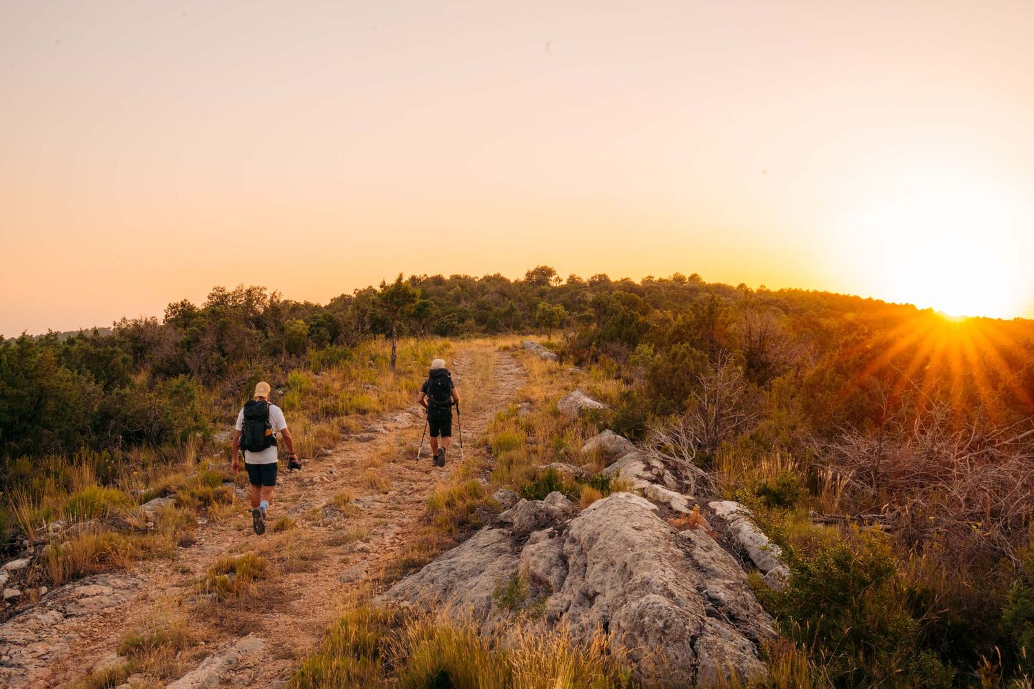 Scenic hiking trail along a mountain ridge at sunset with golden light illuminating the rugged landscape.