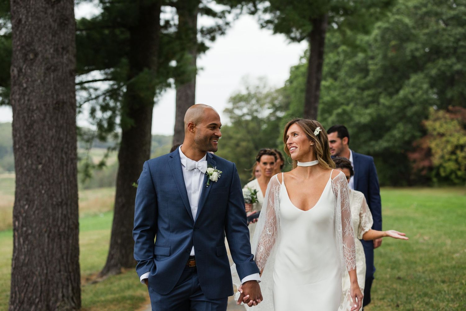 Wedding couple walking together outdoors surrounded by tall pine trees.