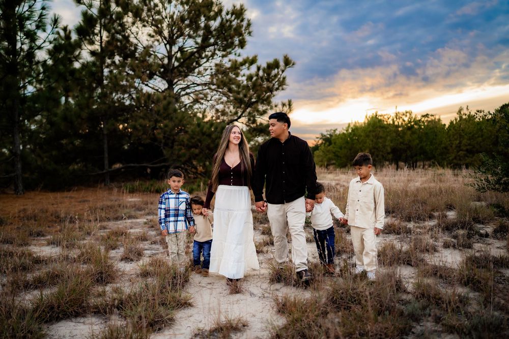 Family of five walking on a sandy path at sunset with trees and colorful sky in background.