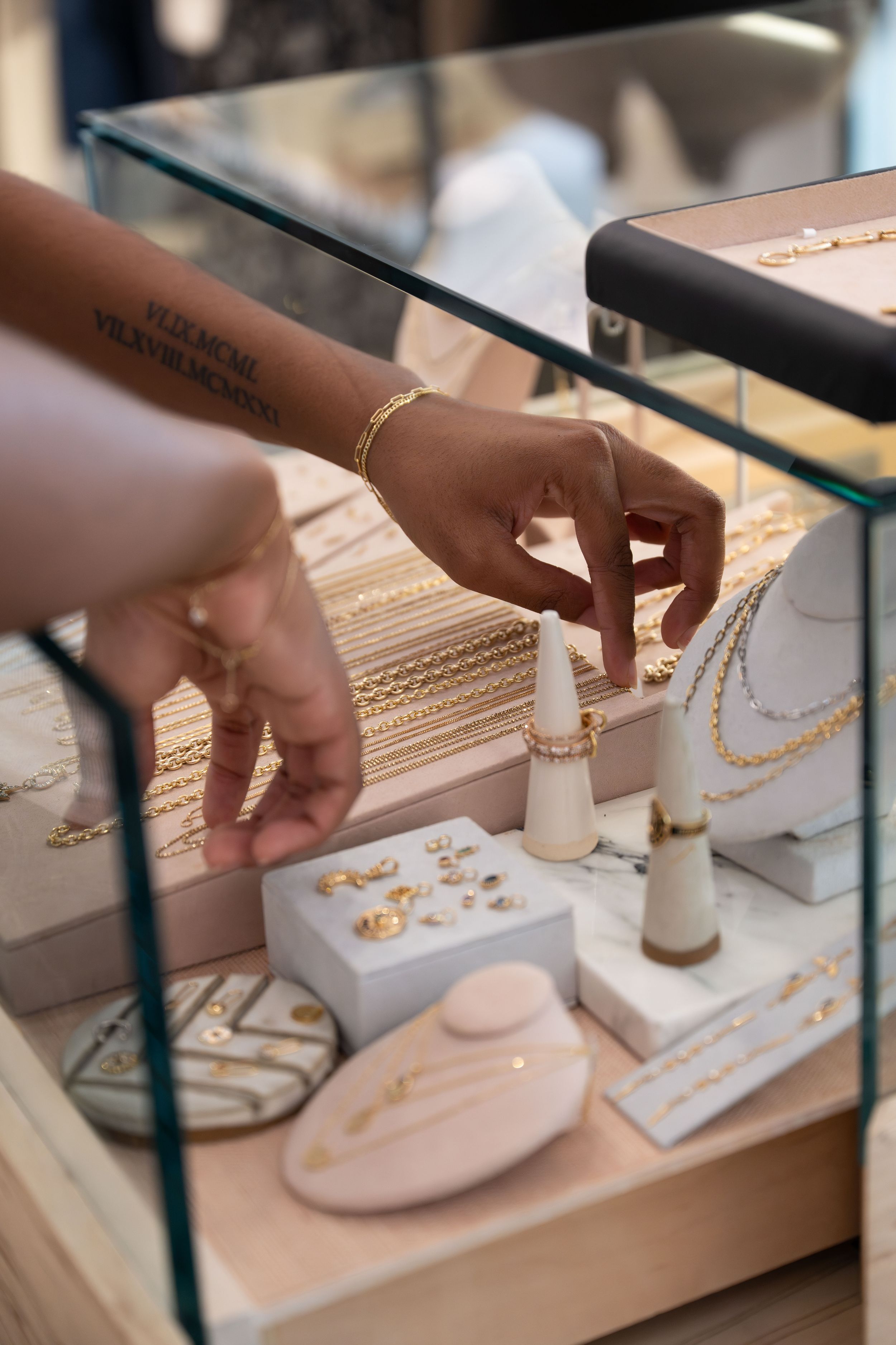 A jeweler arranges gold necklaces and rings on white display stands inside a glass jewelry case.
